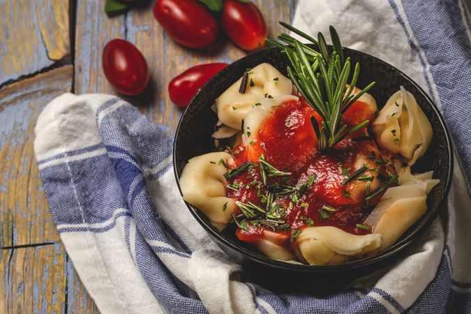 Bowl of delicious ravioli with tomato sauce and rosemary on shabby table