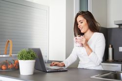 Smiling woman browsing on laptop and sitting on settee
