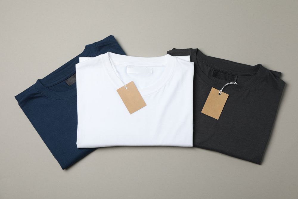 Folded blank t-shirts with tags on gray background, space for text