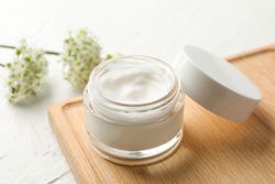 Jar with cream, allium flowers and board on blank background, closeup