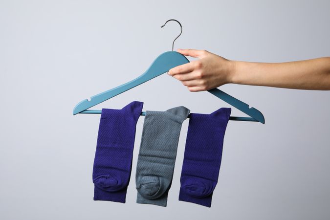 Female hand holds hanger with socks on light gray background