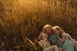 Mother hugging daughters while lying on rye field