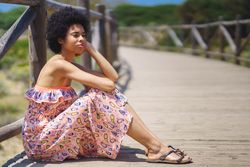 Woman in maxi dress sitting on footbridge in the sun