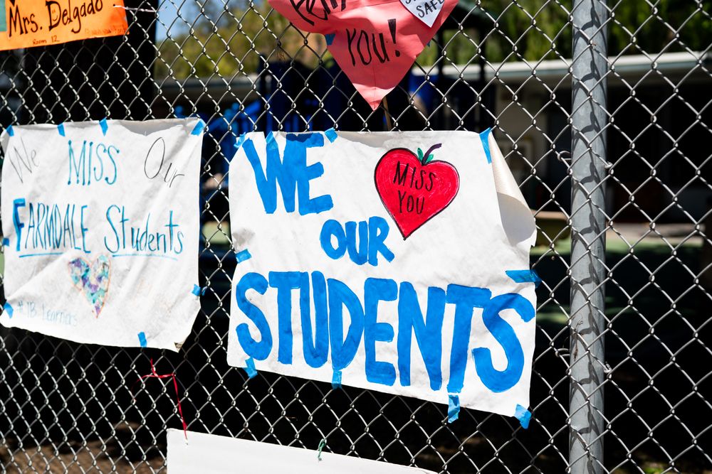 Handmade signs from teachers to students taped to a school fence during distance learning