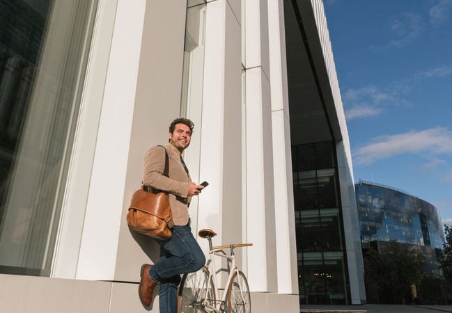 Businessman with smartphone leaning on building on city street
