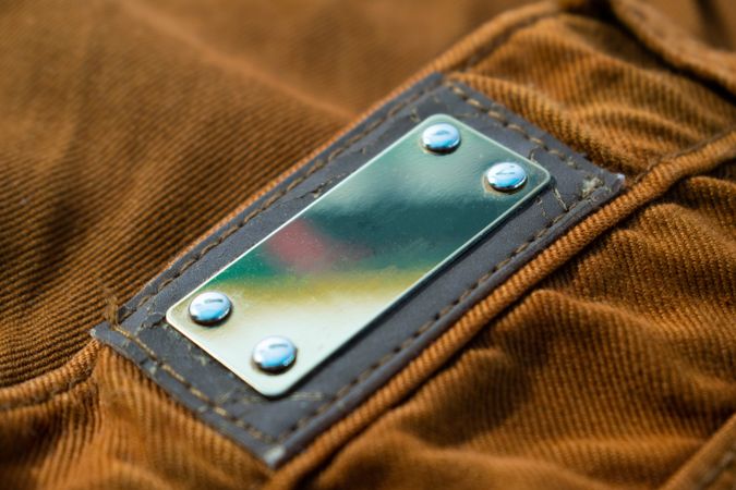 Blank shiny metallic label on bright brown jeans, fabric texture mockup