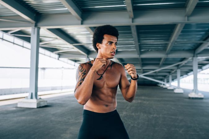 Serious Black male athlete doing boxing training in underpass