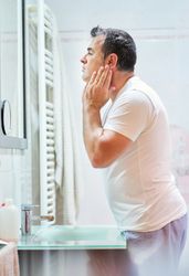 Man touching face in bathroom while looking in mirror