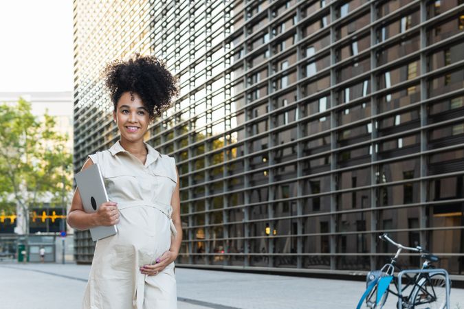 Smiling Black woman with laptop coming out of office building