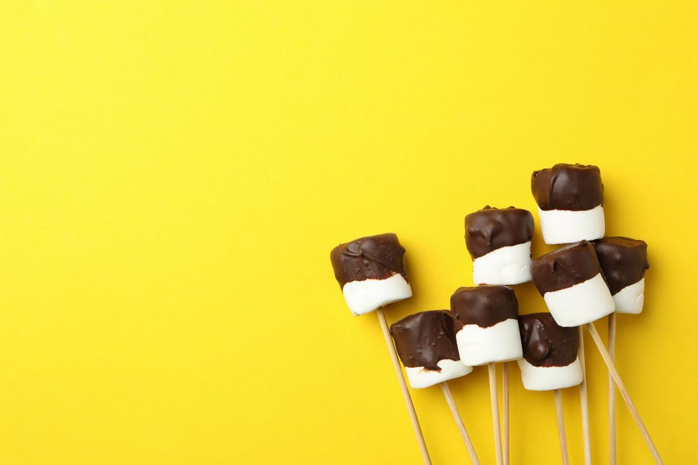 Marshmallows in chocolate on yellow background, space for text