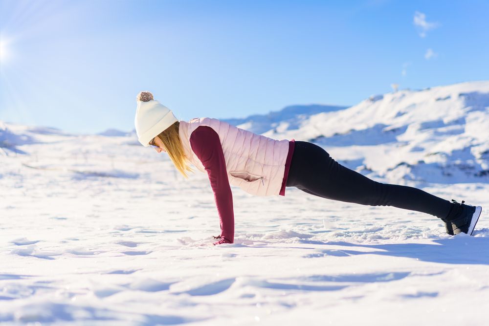 Side view of woman in snowsuit doing pushup on snowy mountain