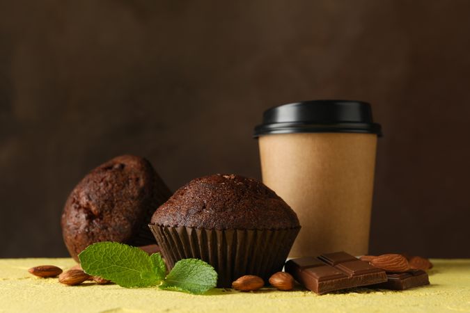 Composition with tasty muffins and paper cup on yellow table