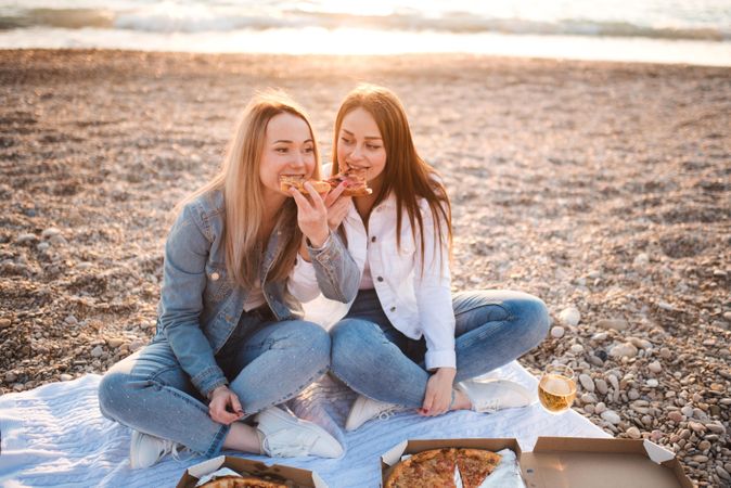 Two women wearing jeans eating pizza at the beach