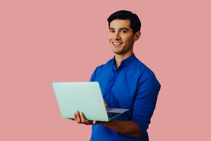 Happy Latino man holding laptop in pink room