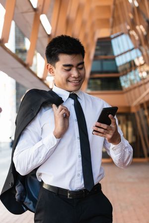 Cheerful Asian male entrepreneur browsing smartphone in city