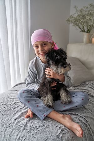 Happy boy in symbolic pink bandana hugging fluffy dog