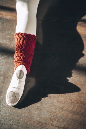 Crop shot from above of ballerina's leg wearing white pointe shoe on wooden floor.