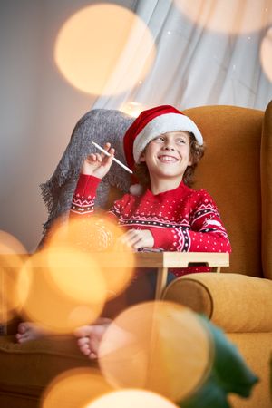 Cheerful boy in Santa hat drawing at home