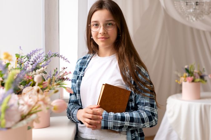 Smiling teen girl holding book standing near flower bouquets.
