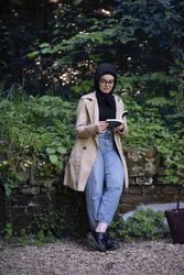 Woman relaxing on a mossy tree in a trench coat with book