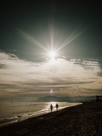 Couple walking on beach against sundown