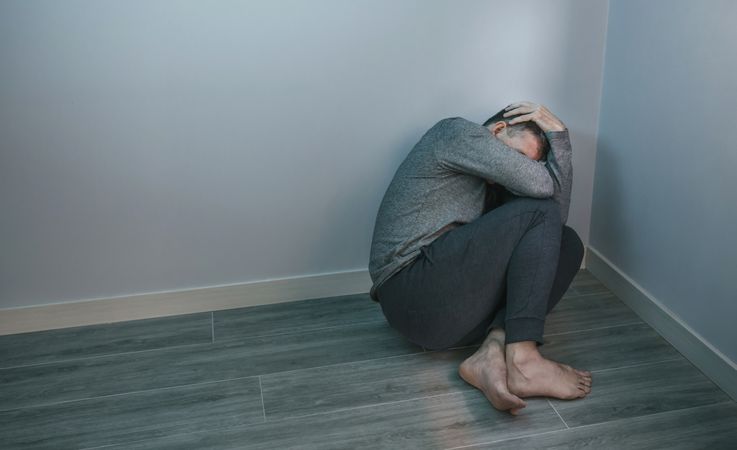Unrecognizable man with problems sitting in the corner of room