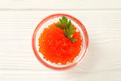 Glass jar with red caviar isolated on wooden table, space for text