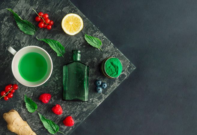 Healthy scene of tea, spirulina powder, nettle leaves, ginger on marble slap on dark background