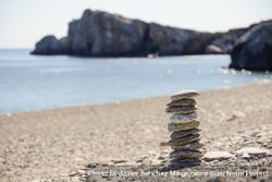 Pebbles balancing on the sandy beach with cliffs in background 5pGzx0