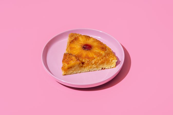 Pineapple cake slice on a plate isolated on a pink background