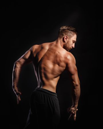 Bodybuilder practicing poses ahead of competition in dark studio