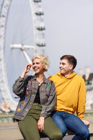 Male and female friend sitting in front of London Eye