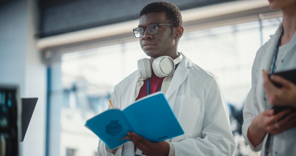 Portrait of a Young Black Male Engineering Student Asking Questions, Taking Notes in a Laboratory.