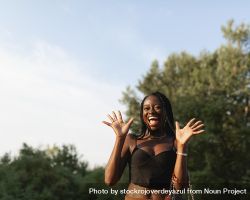 A young Black woman, with braids in her hair, gesticulates and gets excited, during a walk in the park at sunset 5kRRoW