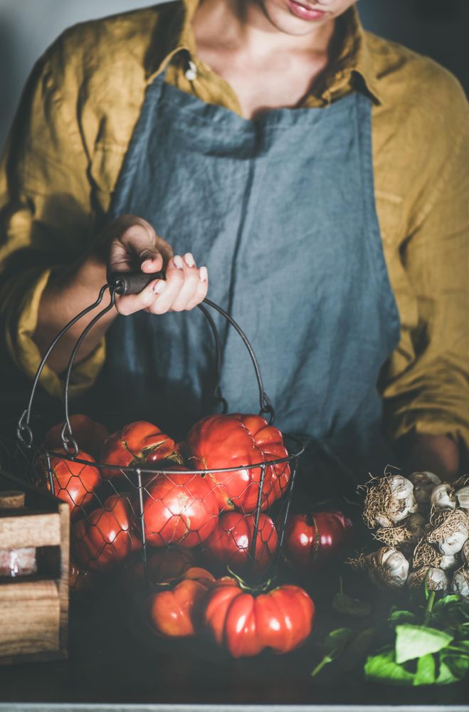 Woman in yellow holding wire basket full of tomatoes