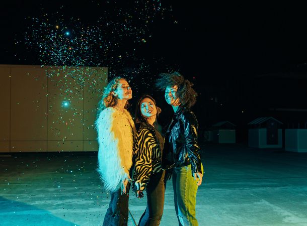 Group of female friends lit in green blue light at night with confetti falling