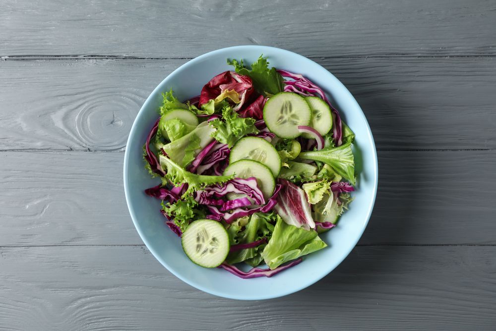 Plate with fresh salad on wooden background, space for text
