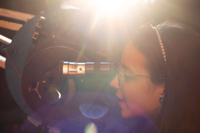 Girl looks through telescope with bright sunlight flare.