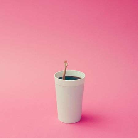 Coffee cup with female doll hand on pink background, with copy space