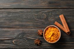 Bowl of turmeric with cinnamon sticks and anise, copy space