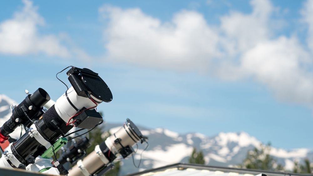 Telescopes on observatory rooftop with mountain view.