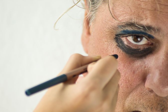 Hand applying dark and blue eyeshadow to middle aged man's eye