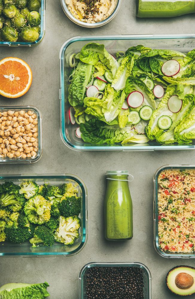Variety of vegetable dishes in glass containers with bottles of dressing, vertical composition
