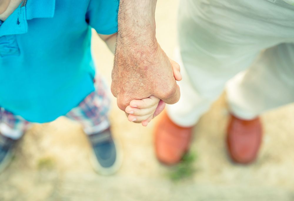 Child holding hand of older man in the nature