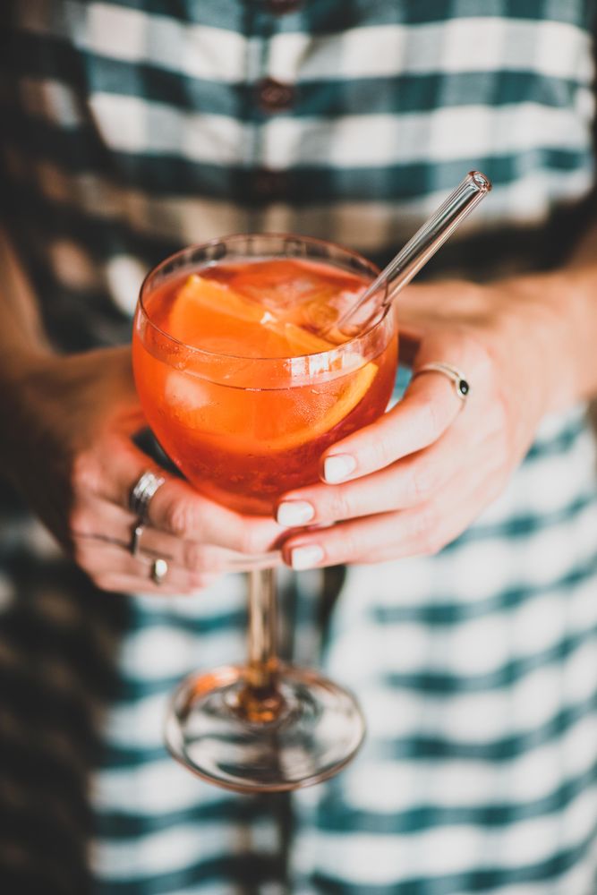 Young woman in checkered dress holding aperitif with orange slices and glass straw