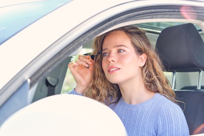 Content woman applying mascara in car