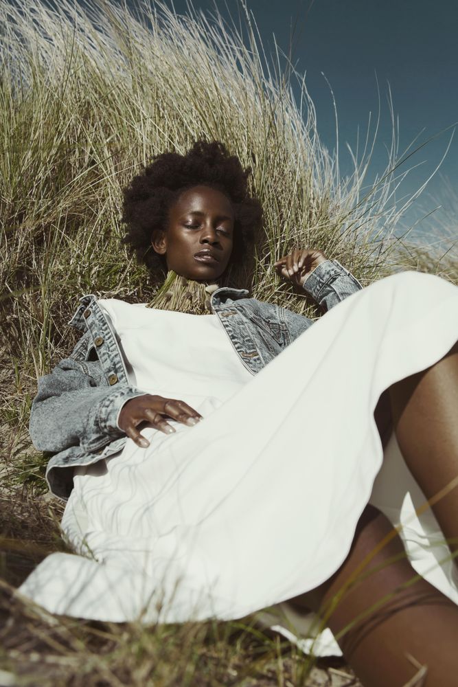 Woman in light dress and denim jacket laying on brown grass