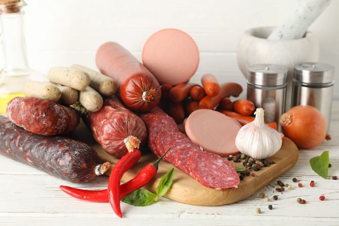 Variation of cured meats with peppers and spices on wooden board in kitchen