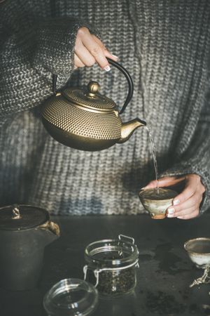 Woman in cozy sweater pouring from traditional Japanese tea set
