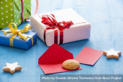 Three presents wrapped in colorful paper next to cookies on a blue table 0ynZq5